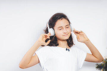 Photo of young happy beautiful caucasian teenager girl listen music in headphones on a white color background. Teenager stock photo. Beautiful brunette girl in a white T-shirt.