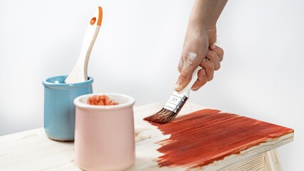Women's hand-painted wooden furniture with a brush. Close-up hand on a white background. Do-it-yourself renovation of the house concept. Banner format.