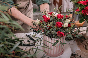 Florist make gift bouquets in hat boxes. Graceful female hands make a beautiful bouquet. Florist workplace. Small business concept. Front view. Flowers and accessories.