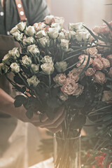 Woman florist hands holding a big bouquet of roses. Florist workplace. Small business concept. Flowers and accessories shop. Vertical shot