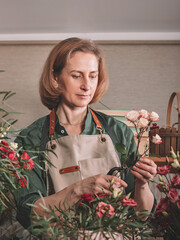 Beautiful woman florist making a gift bouquet of roses. Florist workplace. Small business concept. Front view. Flowers and accessories.