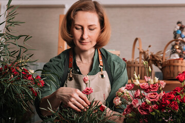 Beautiful woman florist making a gift bouquet of roses. Florist workplace. Small business concept. Front view. Flowers and accessories. Selective focus