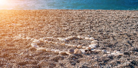 Love heart shape on sand made out of white pebbles, symbol of love on the beach with sea background. Valentine day love symbol of heart shape, love, feelings. Romantic couple trip on Valentine's Day.