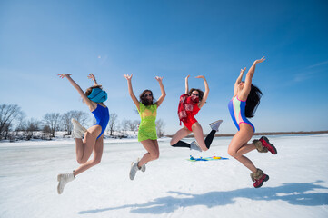 Four Caucasian women in swimsuits are fooling around on a snowy beach. Winter fun.