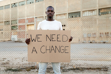 Young African American man looking at camera holds we need a change banner protest for black lives...