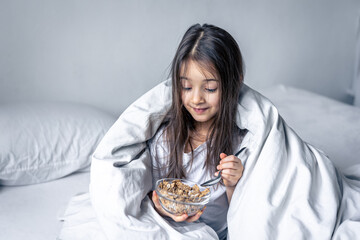 Little cute brunette girl in a white bed has breakfast cereal.