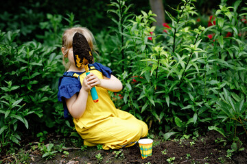 Little preschool girl planting seedlings of sunflowers in domestic garden. Toddler child learn...