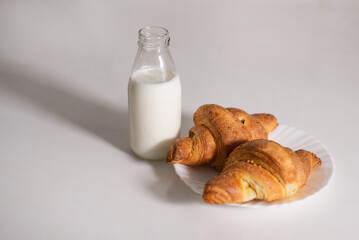 Fresh croissant and bottle of milk on white table. Continental breakfast