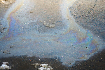 Colored spots of oil or gasoline on the asphalt as a texture or background. Melting snow with simultaneous pollution from the oil spill of the parking lot. Selective focus