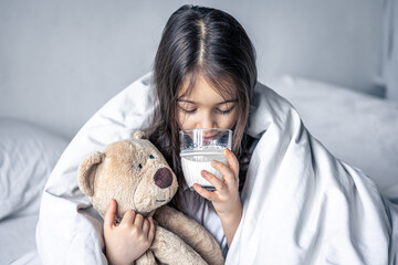 A little cute girl in bed with a plush and a glass of milk.