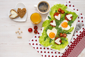 Breakfast on Valentines Day. A plate of fried heart-shaped eggs, cheese and tomatoes, coffee and juice, bread and butter on a white wooden table and the inscription I love you Breakfast for loved one