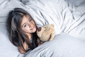 Little cute girl in bed with a teddy bear early in the morning, copy space.