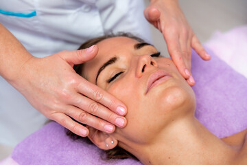 Relaxing massage. European woman getting facial massage in spa salon, side view