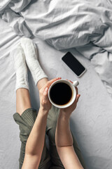 Fototapeta na wymiar Cup of coffee in bed in female hands, top view.