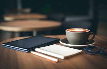 Work from home, desk office with digital tablet, blank notepad, eye glasses, mobile phone and coffee cup with heart shape of latte on wooden table