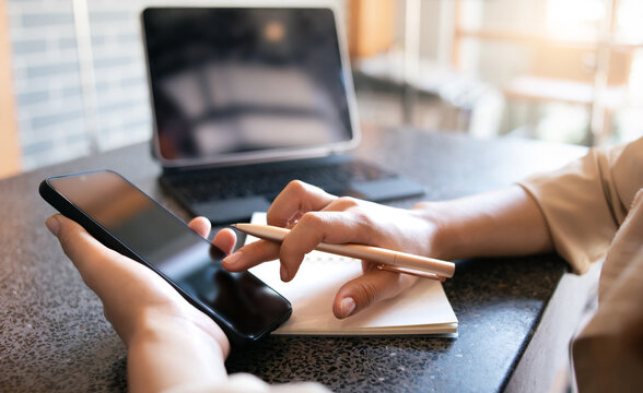 Young asian woman using mobile phone working or shopping online with laptop computer on desk. Closeup photo and select focus on hand