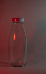 A glass milk bottle with a white lid on a dark background. Neon red lamp. Blank mock up