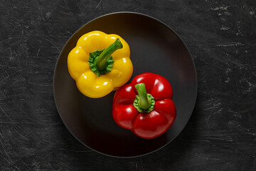 Peppers two bulgarian sweet yellow and red on gray plate top view dark background, with space to copy text.
