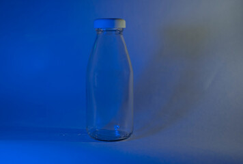 A glass milk bottle with a white lid stands on a dark background. Neon blue lamp. Blank mock up