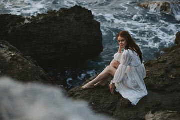 A woman in a white wedding dress is sitting barefoot on a wave cliff