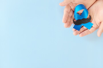 Top view of male hands holding light blue ribbon with mustache. Father's day, Men's Health and Prostate Cancer Awareness and Movember concept. 