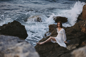 Woman in white dress sits on a stone near the ocean waves travel nature