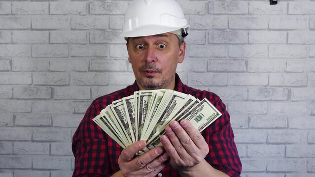 Portrait of a cheerful man in a construction helmet throwing money . Against the background of a brick wall . The concept of financial success. Remuneration of labor.