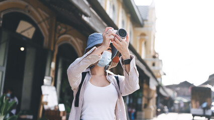 Young adult asian woman backpack traveller wear face mask take a photo by camera.