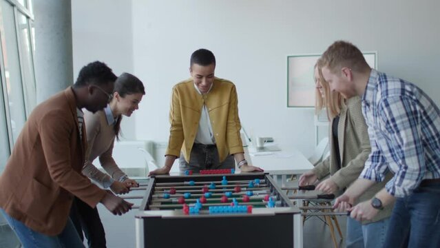 Young handsome casual multiethnic business people playing table football and relaxing at office