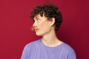 Fototapeta na wymiar Young curly-haired man in yellow glasses purple t-shirt emotions red background