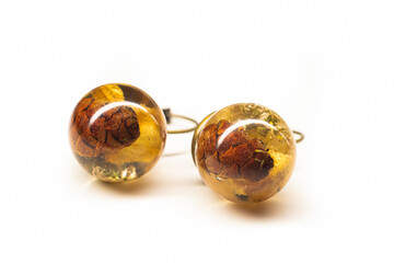 Sphere ball earrings with natural plants. Epoxy resin handmade jewelry closeup. Brown and yellow growth. Selective focus on the details, object isolated on white background.