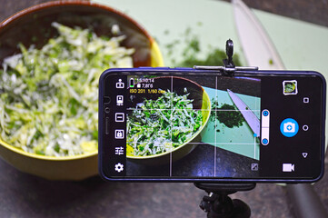 shooting on a smartphone preparing a salad of fresh cabbage, green onions and cucumbers with dill in a round bowl