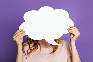 Woman holding blank speech bubble paper isolated on purple background. White paper cloud for text...