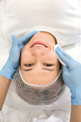 Dermatologist cosmetologist wiping the face of a female client preparing for a facial cleansing...