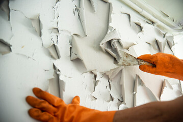 worker hands in glove peeling wall paint off
