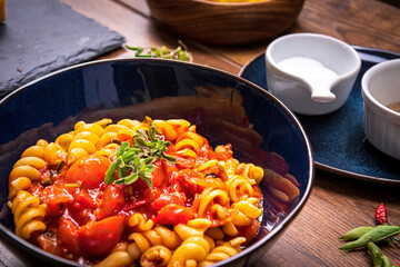 pasta in a blue cup with tomato sauce on a wooden table