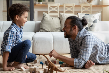 Joyful laughing African American small cute child boy enjoying communicating with millennial...