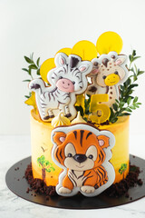 Birthday safari cake with yellow cream cheese frosting with gingerbread cookies. Africa cake with tiger and zebra cookies on the white background