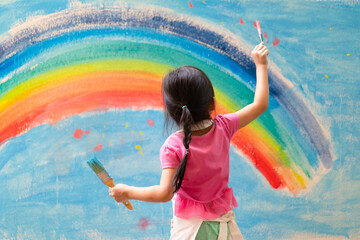 Unidentified little girl is painting the colorful rainbow and sky on the wall and she look happy...