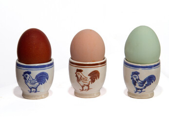 Three egg cups, decorated with a rooster, eggs in three different colors, laid by three types of...