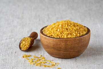 Uncooked bulgur in wooden bowl on linen cloth background. Bulgur wheat grains .Closeup