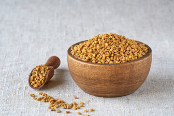Fenugreek seeds in wooden bowl on linen cloth. Close up