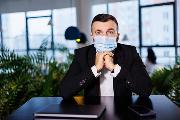 Handsome young man in a mask working in a cafe with a laptop during the coronavirus pandemic.
