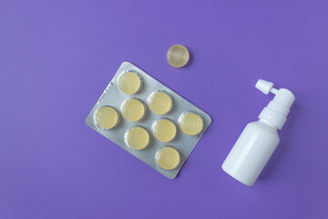Top view of white ear spray bottle and blister of yellow cough drops. Purple background. Health care in the spring time 