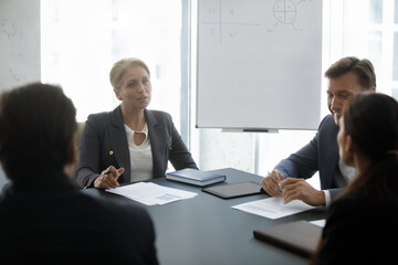 Serious confident mature businesswoman speaking on meeting, negotiating on deal with business...