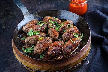Traditional Croatian cevapcici spicy meat ball rolls with parsley and hot ajvar served as close-up in a skillet