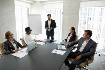 Business group leader holding corporate meeting in conference room, talking to diverse team,...