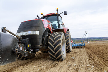 Obraz premium A large red tractor close-up with sowing equipment stands in a field.