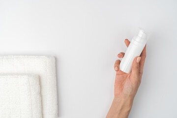 A close shot of the thin graceful hands of a girl with a nude manicure holds a bottle of foam for washing, cleansing the skin of the face, on a white background. Fresh towel.