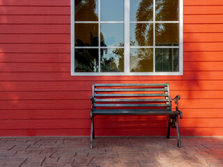 Empty black wrought iron bench decorated in front of the red wood plank building near the white window glass.